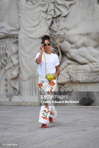 Ellie Delphine wears white and green squared sunglasses, gold earrings, gold chain necklaces, a white t-shirt, white latte with embroidered orange...