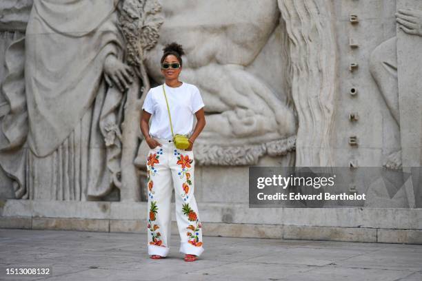 Ellie Delphine wears white and green squared sunglasses, gold earrings, gold chain necklaces, a white t-shirt, white latte with embroidered orange...