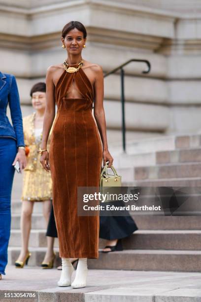 Liya Kebede wears gold earrings, a gold large lips metallic necklace from Schiaparelli, a dark brown velvet halter-neck / cut-out chest / tube long...
