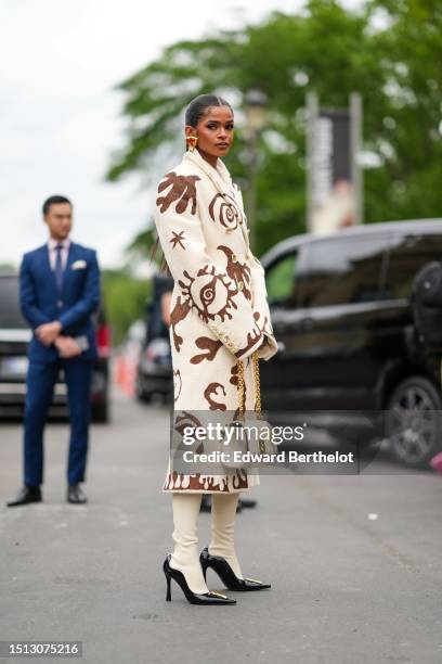 Guest wears gold oversized red lips earrings from Schiaparelli, a white latte with brown print pattern fluffy long coat from Schiaparelli, a white...