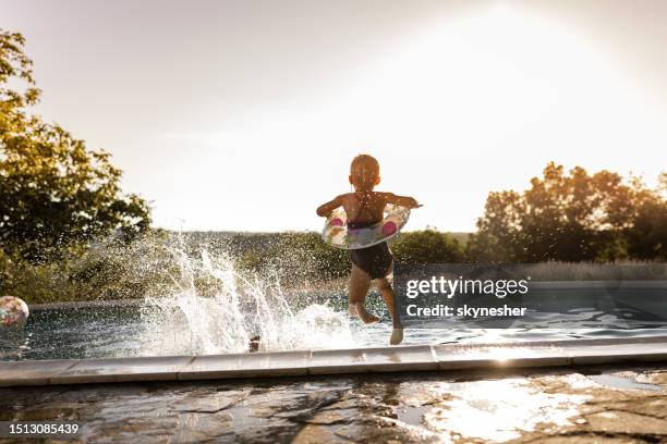 back view of playful kids jumping in the pool at the backyard. - jump in pool stockfoto's en -beelden