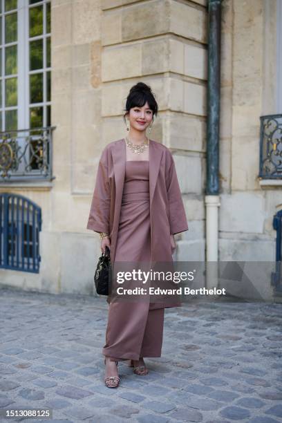 Guest wears gold and diamonds pendant logo earrings from Dior, a gold with white and green pendants chains necklace from Dior, a pale burgundy...