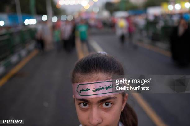 Young Iranian girl wearing a religious headband with an Arabic script that is an attribute of Imam Ali looks on while participating in a rally...