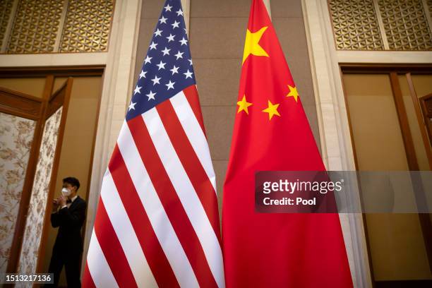 Staff member wearing a face mask walks past United States and Chinese flags set up before a meeting between Treasury Secretary Janet Yellen and...
