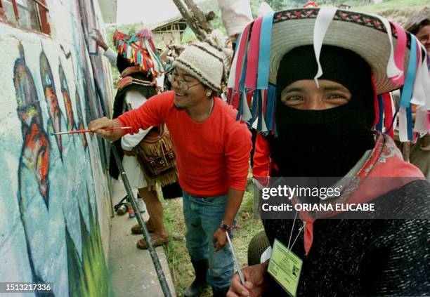 Jose Calarza de la organizacion chicana Big Frente Zapatista y dos miembros del Ejercito Zapatista de Liberacion Nacional pintan un mural en el...