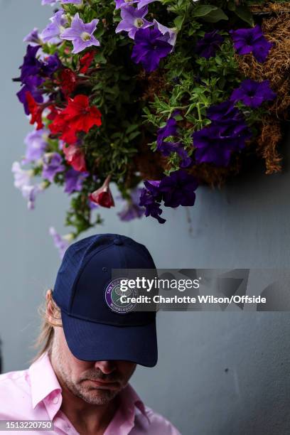 Man with a Wimbledon cap stands beneath a hanging basket of flowers during day four of The Championships Wimbledon 2023 at All England Lawn Tennis...