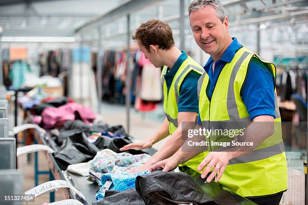 two men sorting clothes on conveyor belt in warehouse - textile industry uk stock pictures, royalty-free photos & images