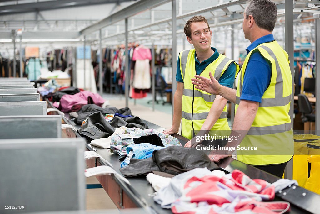 Two men sorting clothes on conveyor belt in warehouse