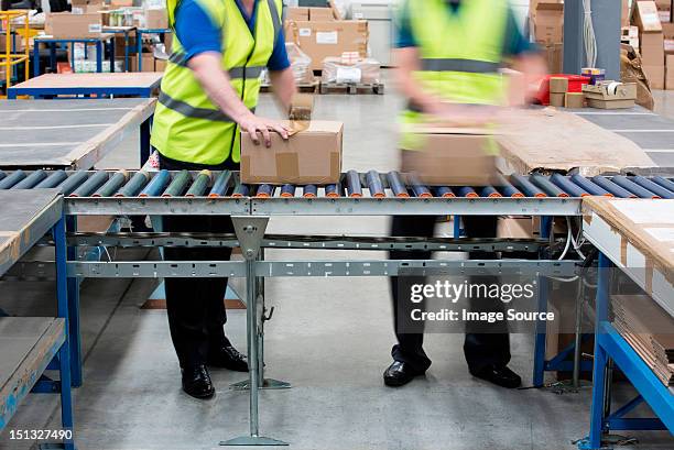 men passing cardboard boxes along conveyor belt - boxes conveyor belt stockfoto's en -beelden