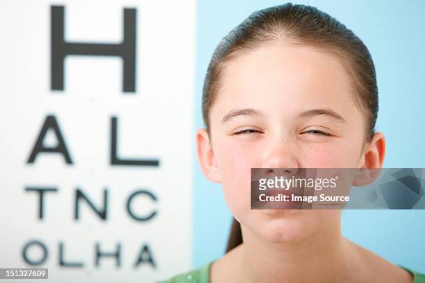 girl squinting with eye chart in background - entrecerrar los ojos fotografías e imágenes de stock