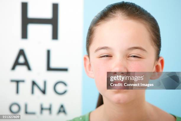 girl squinting with eye chart in background - eye problems stock pictures, royalty-free photos & images