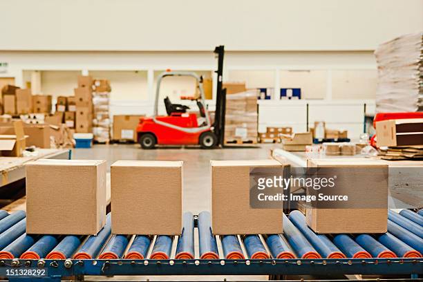 four cardboard boxes on conveyor belt - boxes conveyor belt stockfoto's en -beelden