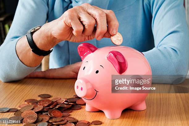 senior woman inserting coins into piggybank - piggybank stock-fotos und bilder