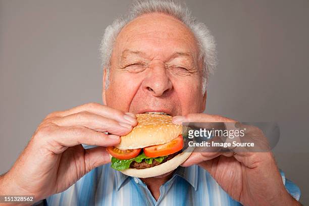 senior man eating burger - man holding a burger stock pictures, royalty-free photos & images