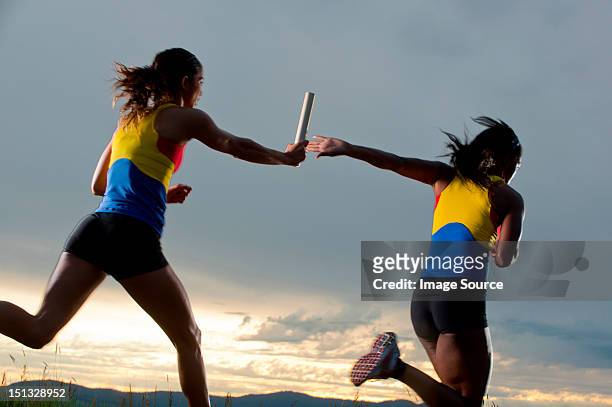 female relay racers passing baton - staffel stock-fotos und bilder