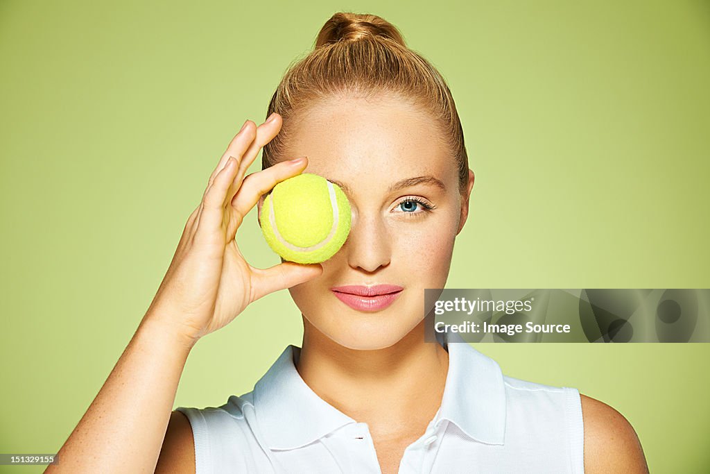 Young woman holding tennis ball over her eye