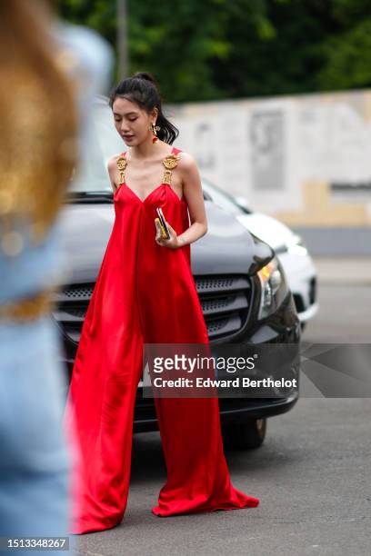 Guest wears gold large eye and white pearls earrings from Schiaparelli, a red flashy with gold large eyes shoulder straps long flowing silk jumpsuit...