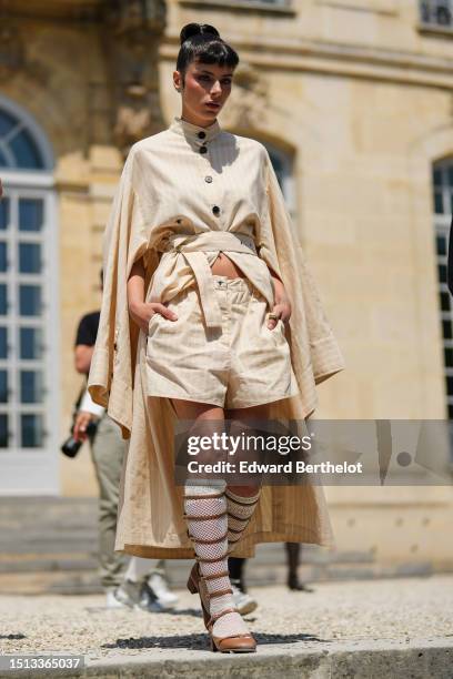 Guest wears a beige and white striped print pattern high buttoned neck bat long sleeves cloak from Dior, beige and white striped print pattern shorts...