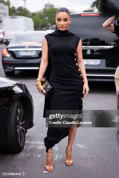 Amina Muaddi wears a black midi dress with gold buttons on the side from Schiaparelli, black Schiaparelli decorated bag, gold heels and gold...