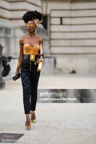 Guest wears a white with camel print pattern silk scarf in the hair, gold metallic glasses from Schiaparelli, gold oversized eye circle earrings from...