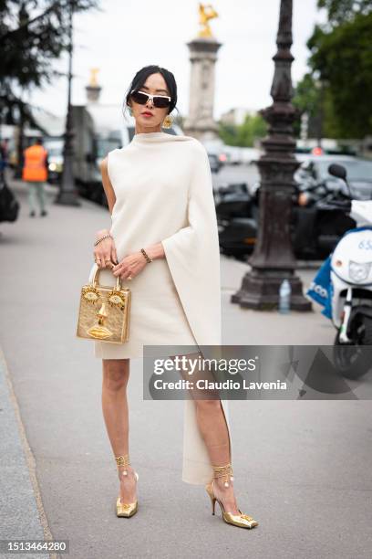 Chriselle Lim wears a cream asymmetric mini dress, gold heels and bag from Schiaparelli, white sunglasses and gold earrings, outside Schiaparelli,...