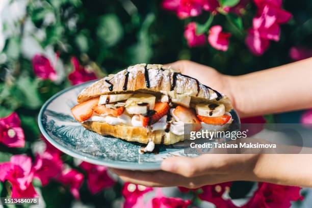 sweet croissant with cream, banana and strawberries covered with chocolate. street café on a sunny day. - banana cream cake stock pictures, royalty-free photos & images