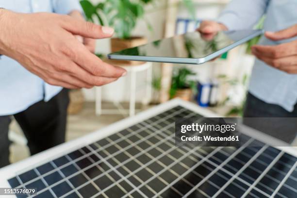 hand of businessman giving tablet pc to colleague over solar panel in office - personne ipad main bureau photos et images de collection