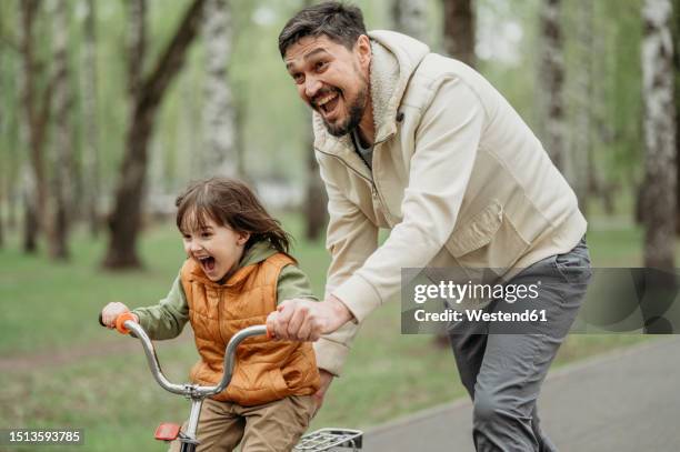 happy father helping son ride bicycle at park - kid riding bicycle stock pictures, royalty-free photos & images