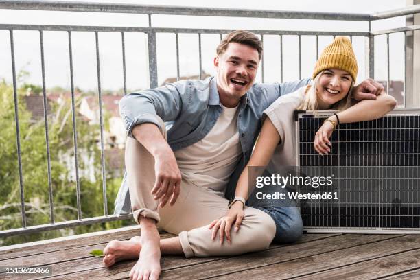 happy couple sitting with solar panel on balcony - kraftwerk stock-fotos und bilder