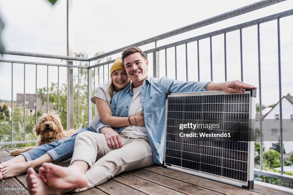 Happy couple sitting with solar panel and dog