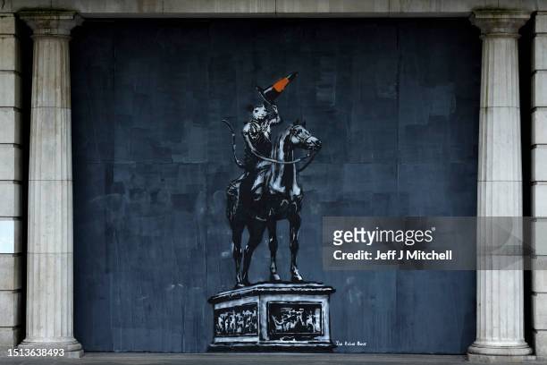 Members of the public walk past work by the street artist The Rebel Bear, a tribute by the Glasgow artist to Banksy, on Argyle Street on July 04,...