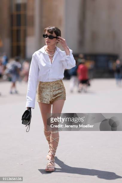 Mary Leest is seen wearing black sunglasses, peal earrings, three pearl necklaces, a white long-sleeved shirt half buttoned, shiny golden sequins...