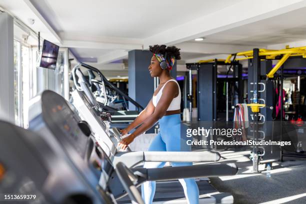 eine schöne junge afrikanische sportlerin hört musik in einem fitnessstudio, während sie auf einem laufband läuft. - black female bodybuilder stock-fotos und bilder