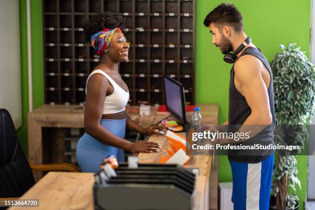 a young sportsman is paying bills with a phone at the reception. - gym receptionist stock pictures, royalty-free photos & images