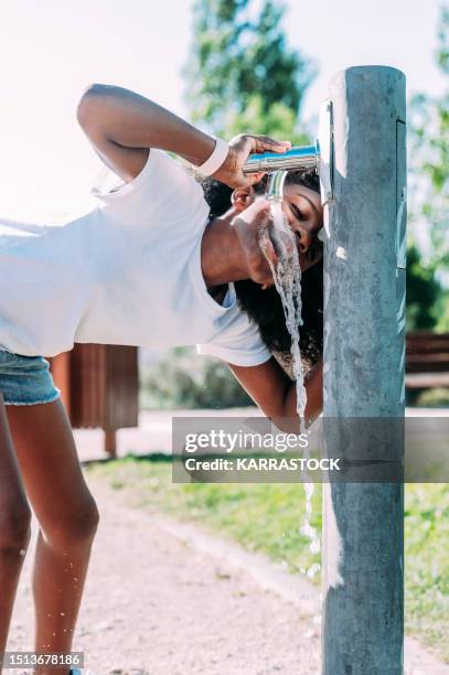 beautiful young afro woman drinking water from a fountain. - african girl drinking water stockfoto's en -beelden