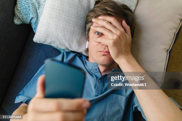 worried man looking at smart phone lying on bed - man with iphone stock pictures, royalty-free photos & images