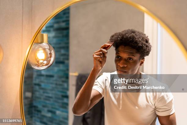 african american man looking at bathroom mirror combing short hair - man combing hair stock pictures, royalty-free photos & images