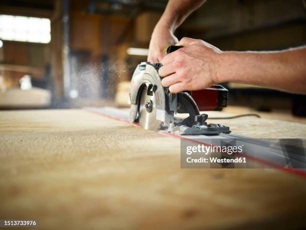 carpenter cutting wooden board with circular saw in workshop - sawing stock pictures, royalty-free photos & images