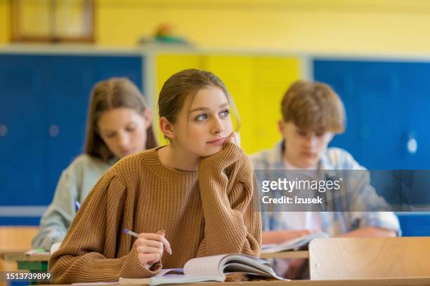pensive teenage girl sitting in the classroom - boy thinking stockfoto's en -beelden