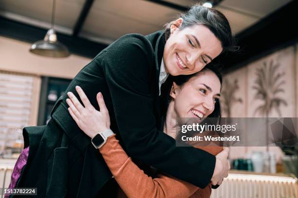 smiling businesswoman embracing friend at cafe - long coat stock pictures, royalty-free photos & images
