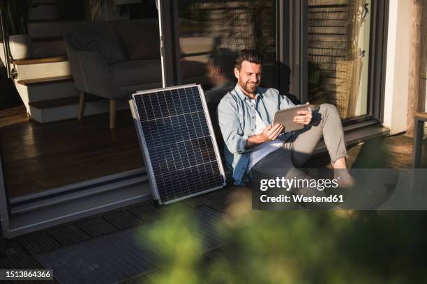 smiling businessman using tablet pc by solar panel on porch - solar panel array front view stock pictures, royalty-free photos & images