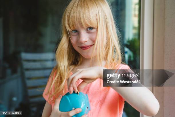 smiling girl saving coin in piggy bank - taschengeld kind stock-fotos und bilder