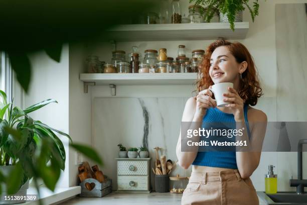 smiling young woman standing with coffee cup at home - women drinking coffee photos et images de collection
