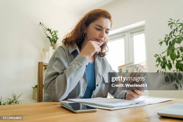 confused young woman calculating financial bills and counting currency at home - contare foto e immagini stock