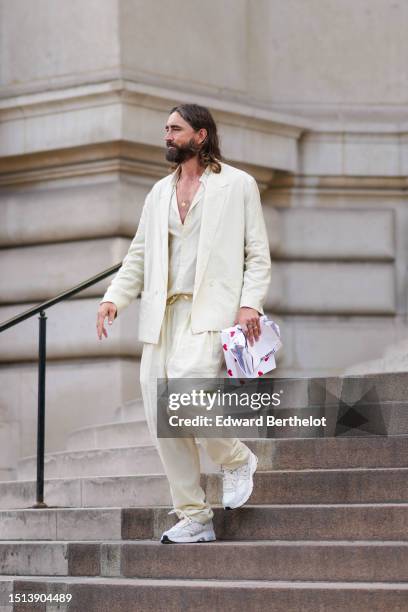 Guest wears a white latte V-neck shirt, a white latte blazer jacket, matching white latte suit large pants, a gold ring, white leather and fabric...