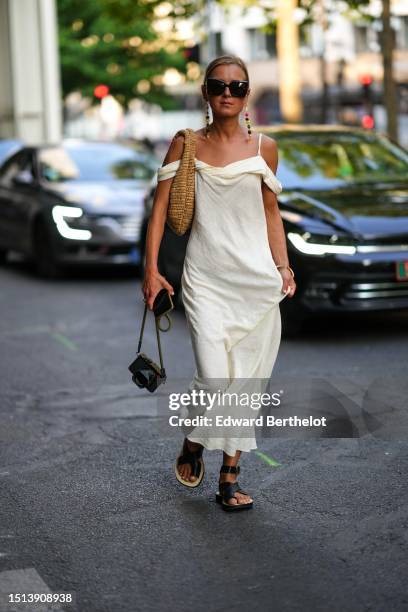 Guest wears black sunglasses, a pale yellow shoulder-off flowing dress, a brown braided wickers shoulder bag, black shiny leather asymmetric toe-cap...