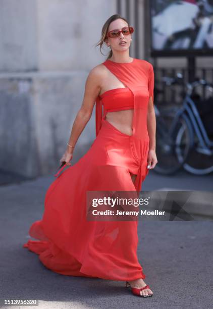 Is seen wearing sunglasses in orange/brown, an asymmetric one shoulder maxi dress with cut-outs and peep toes shoes in red outside during the Georges...