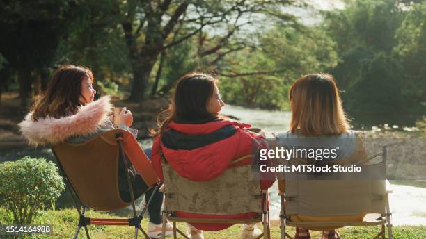 group of happy asian friends talking and drinking a cup of hot coffee for breakfast near stream in vacation with camping caravan at morning. lifestyle travel nature. - human back stock pictures, royalty-free photos & images