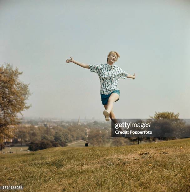 Exterior scene of a female fashion model wearing a pair of blue shorts and a white and blue patterned short sleeved top, she leaps in the air on...