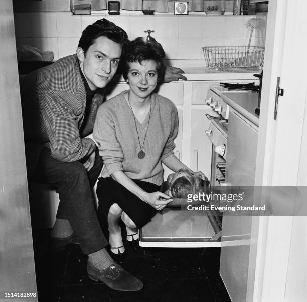 Actor Jeremy Brett with his wife, actress Anna Massey kneeling beside a freshly cooked chicken at their oven, January 1st 1959.